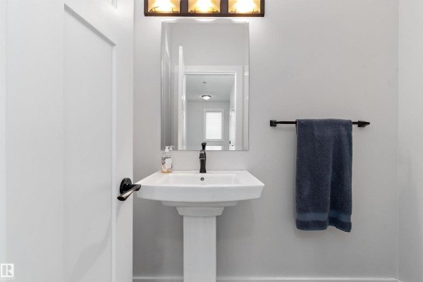 Powder room with pedestal sink, black faucet, mirror, and a dark blue towel. - 5811 Mullen Pl Nw, Edmonton