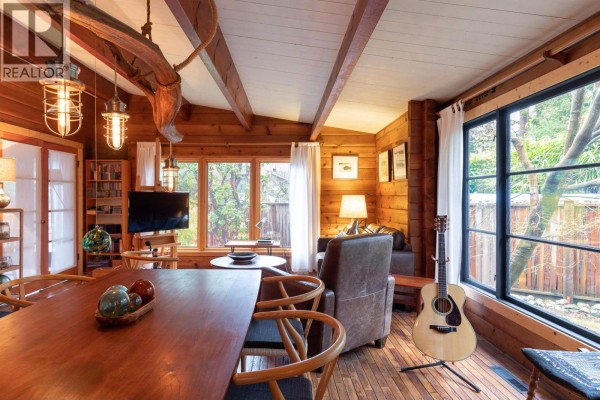 Living and dining space with wood accents, a fireplace, leather armchair, and a view of the outdoors. - 5817 Eagle Island, West Vancouver
