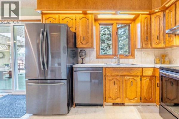 Kitchen with stainless steel refrigerator and dishwasher, oak cabinets, and a window over the sink with a wooded view. - 5825 52 Street, Wetaskiwin