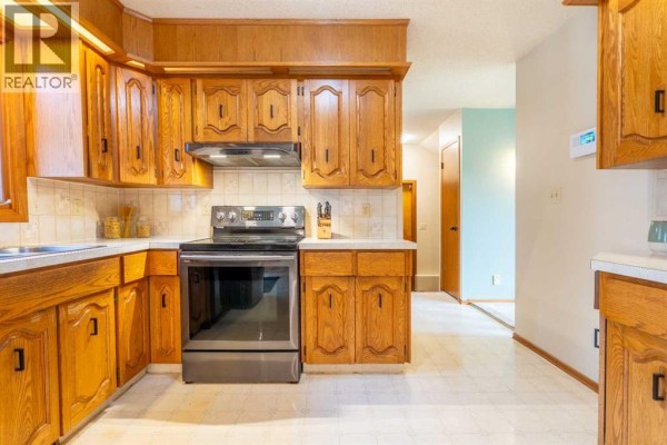 Kitchen with stainless steel stove and range hood, light oak cabinets, white countertop, and a hallway entrance. - 5825 52 Street, Wetaskiwin