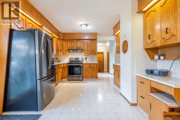 Spacious kitchen with a large stainless steel refrigerator, oak cabinets, stainless steel stove, and a view down a hallway. - 5825 52 Street, Wetaskiwin