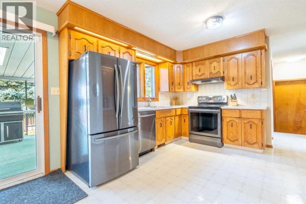 View of the kitchen, showing oak cabinets, stainless steel appliances, and a sliding glass door leading to an outdoor deck. - 5825 52 Street, Wetaskiwin