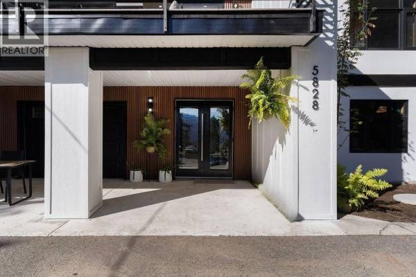 Entrance to the home with glass double doors, flanked by white pillars and vertical wood paneling. - 5828 Brown Place, Peachland
