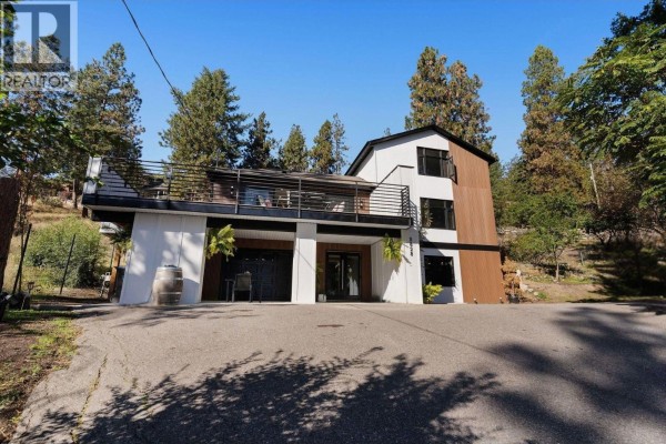 View of the modern home from a driveway, showing multiple levels and surrounding pine trees. - 5828 Brown Place, Peachland