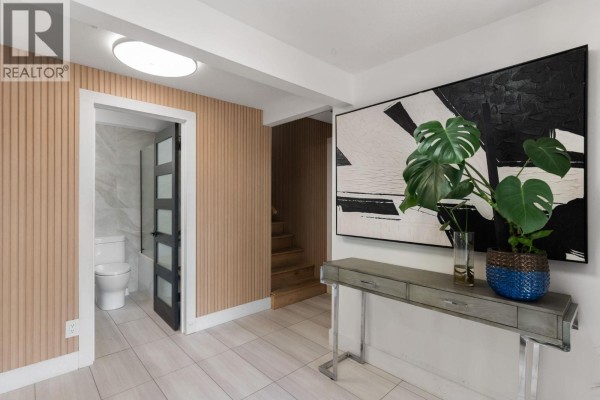 Interior hallway with beige vertical wood paneling, a half-glass door to a white tiled bathroom, and a console table. - 5828 Brown Place, Peachland