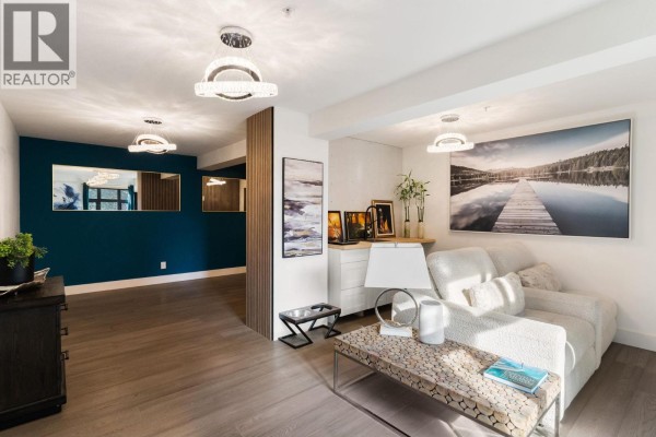 Living room with a sectional sofa, modern coffee table, and artwork, next to a hallway with dark blue walls. - 5828 Brown Place, Peachland