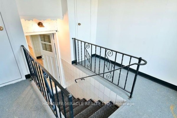 Indoor view of a stairwell with white tiled walls and a black metal railing. - 584 Montgomery Street, Oshawa
