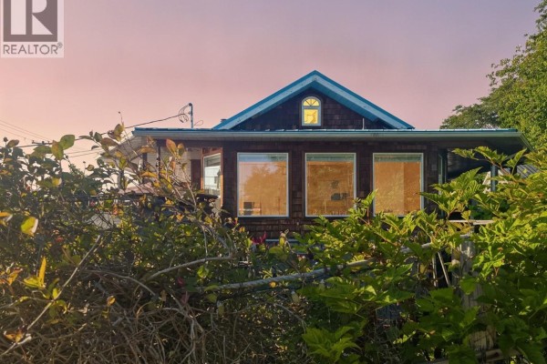 Rear exterior of a house with wood siding and multiple windows, surrounded by foliage. - 585 1st St, Sointula