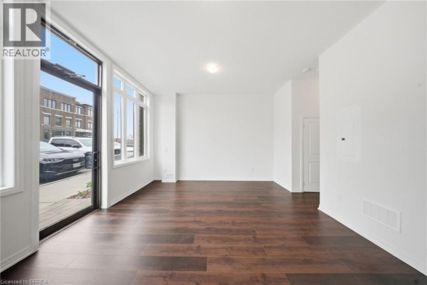 Dining area with dark wood floors, white walls, and a large window. - 585 Colborne Street E Unit# 107, Brantford