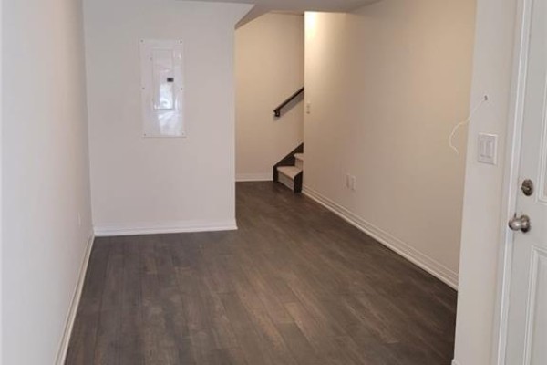 Interior view of a room with dark wood laminate flooring and a staircase. - 585 Colborne Street E Unit# 913, Brantford