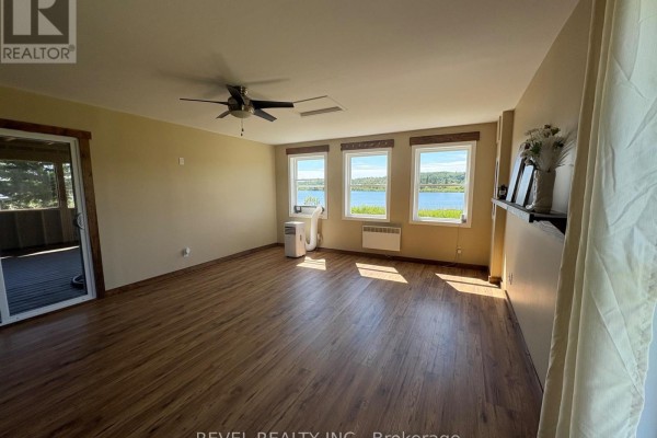 Living room with light wood-look laminate flooring, a ceiling fan, and three windows offering a lake view. - 585 Conc 6 & 7 Concession, Cochrane