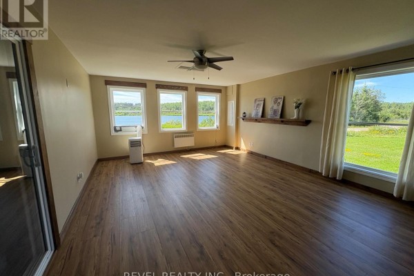 Spacious living room with light wood-look laminate flooring, ceiling fan, and large windows with a view of nature. - 585 Conc 6 & 7 Concession, Cochrane