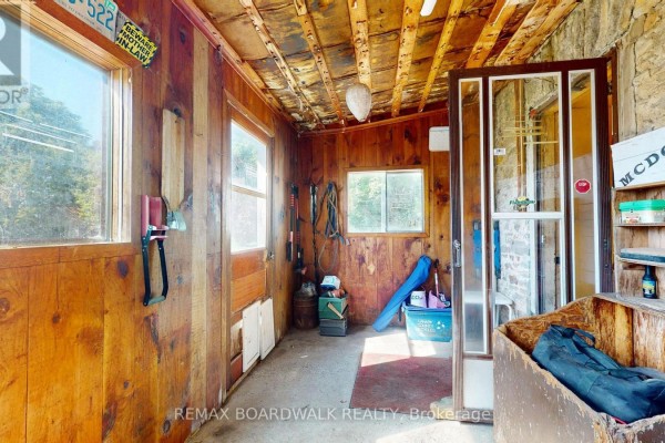 Interior of a rustic room with wood-paneled walls, concrete floor, and windows, featuring stored items. - 585 Fallbrook Road, Tay Valley