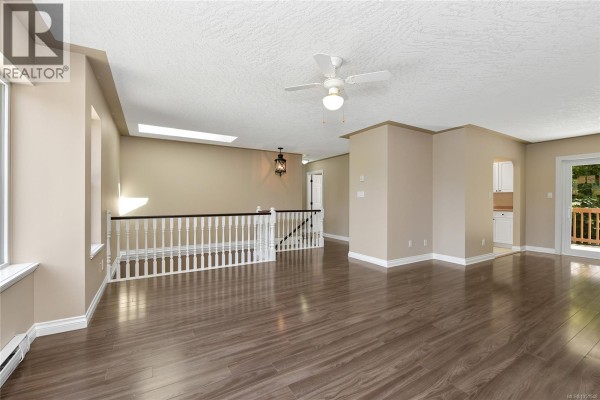 Living room with dark wood floors, a white railing, skylight, and access to a deck. - 585 Hansen Ave, Langford