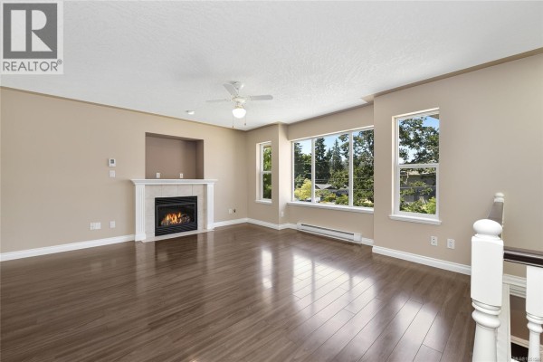 Living room featuring a white fireplace, large windows with green tree views, and wood floors. - 585 Hansen Ave, Langford