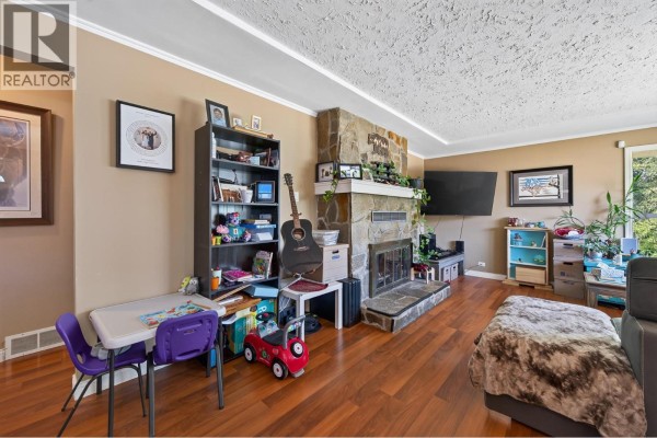 Living room with a stone fireplace, bookshelves, children's play area, and wood flooring. - 5855 Dallas Drive, Kamloops