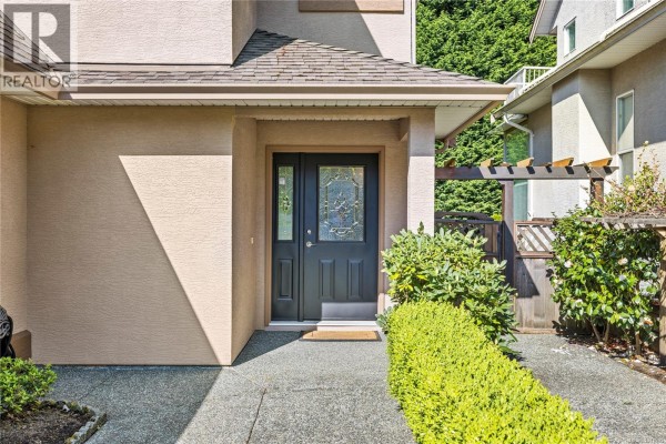 Close-up of a dark gray front door with leaded glass side panels and green shrubbery. - 5857 Quarry Cres, Nanaimo