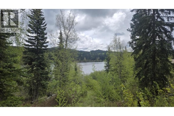 View through bare trees of a cloudy sky over a vast, frozen lake surrounded by forested hills. - 5858 Mahood Lake Road, Lone Butte