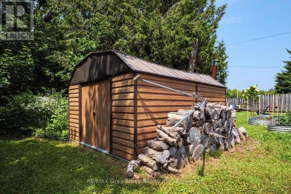 Close-up view of the wooden shed with a metal roof and stacked firewood beside it. - 586 Dawson Street S, South Bruce Peninsula