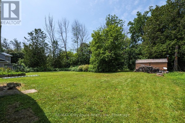 Expansive grassy backyard with mature trees, a shed, and garden beds in the distance. - 586 Dawson Street S, South Bruce Peninsula