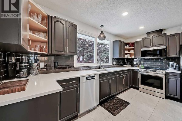 Modern kitchen with dark cabinets, white countertops, and stainless steel appliances. - 5864 Dalford Hill Nw, Calgary
