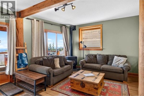 Living room with gas fireplace, two sofas, wood coffee table, and a large window with mountain view. - 5873 Snow Pines Crescent Unit# A, Big White