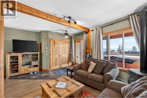 Living room with television, entertainment unit, wood interior doors, and large window with mountain view. - 5873 Snow Pines Crescent Unit# A, Big White