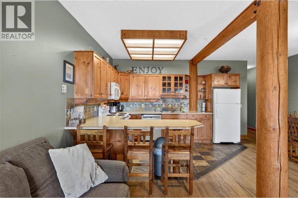 Kitchen with light wood cabinets, granite countertops, tile backsplash, and breakfast bar with stools. - 5873 Snow Pines Crescent Unit# A, Big White