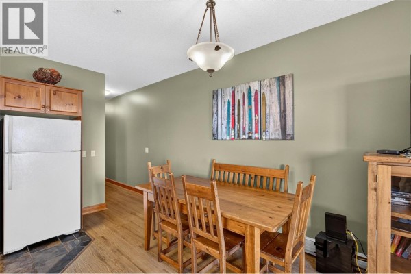 Dining area with wooden table and chairs, beside a refrigerator and a wall-mounted art piece. - 5873 Snow Pines Crescent Unit# A, Big White