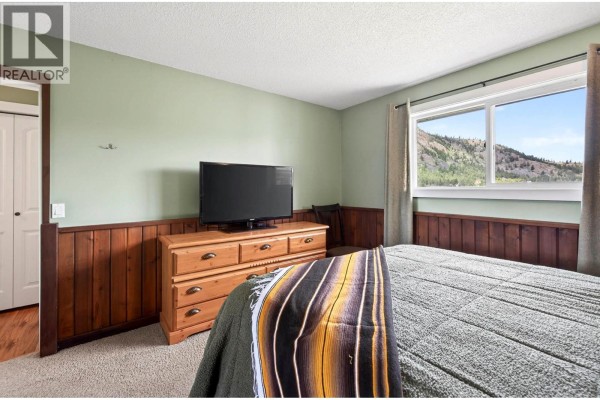 Bedroom with a large window, green walls, wood wainscoting, and a television on a dresser. - 5890 Todd Road, Kamloops