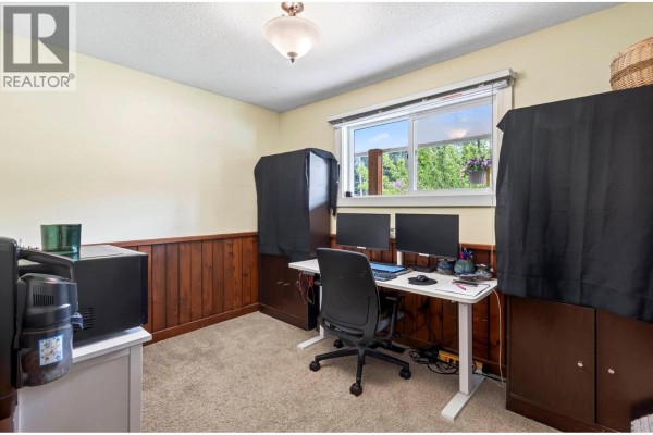 Home office with a desk, dual monitors, chair, and wood wainscoting. - 5890 Todd Road, Kamloops