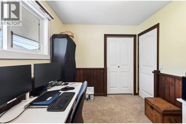 Home office with a desk, computer monitors, closet doors, and a storage chest. - 5890 Todd Road, Kamloops
