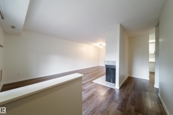 Living room with white walls, dark wood floors, and a brick fireplace. - 5898 172 St Nw, Edmonton