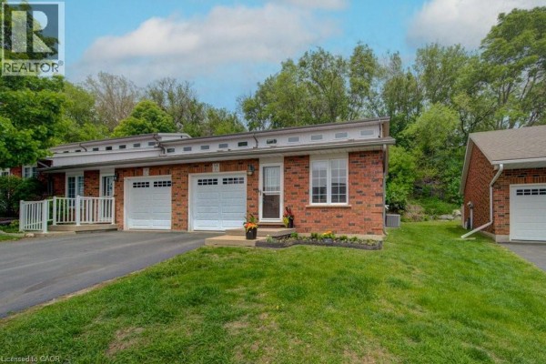 Front view of brick townhouses with white garage doors and manicured landscaping. - 58d Harris Avenue, Brantford