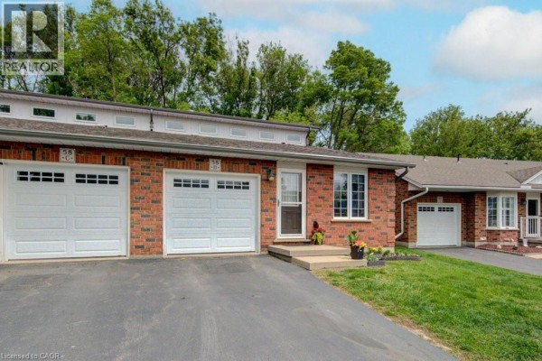 Front exterior of brick townhouses with garages and surrounding trees under a blue sky. - 58d Harris Avenue, Brantford