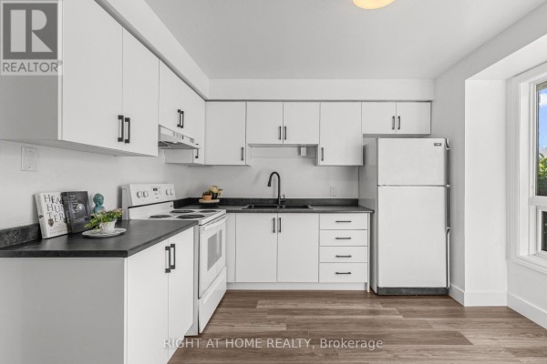 L-shaped kitchen with white cabinets, black countertops, white appliances, and view to dining area. - 59 - 550 Second Street, London East