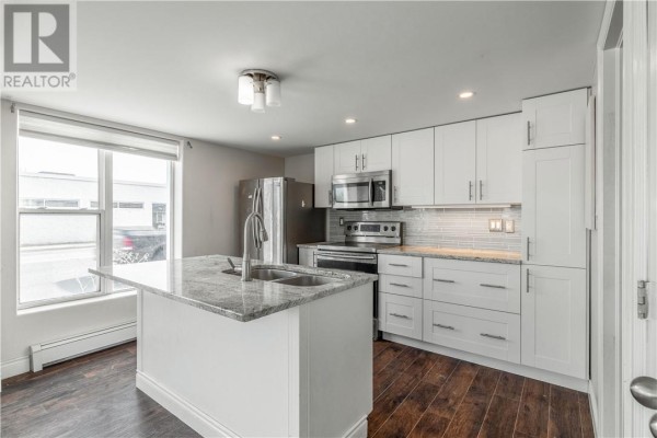 Close-up of the kitchen with granite countertops, white cabinets, and natural light from the window. - 59-61 Lorne Street, Sudbury
