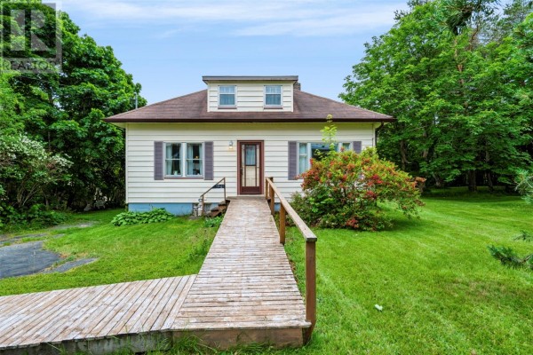 Front view of a light-colored house with a wooden walkway leading to the entrance, surrounded by green lawn and trees. - 59-65 Cross Road, Bay Roberts