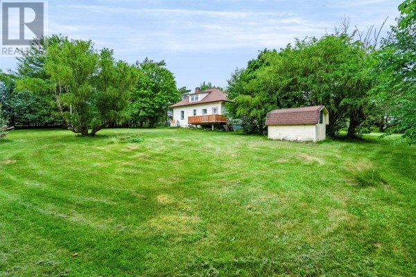 Wide shot of a green lawn with a house and small shed in the background, surrounded by mature trees. - 59-65 Cross Road, Bay Roberts