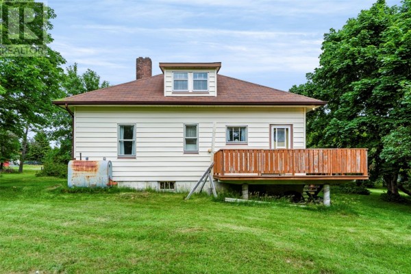 Rear view of a light-colored house with a wooden deck and chimney, situated on a grassy lawn. - 59-65 Cross Road, Bay Roberts