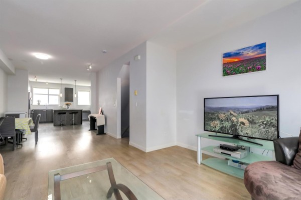 Living area with a large television on a stand, dining area, and kitchen in background. - 59 8355 164 Street, Surrey