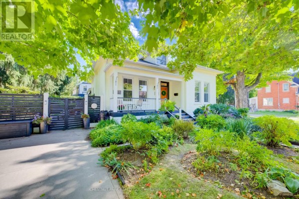 Exterior view of a yellow house with a covered porch, wooden front door, and manicured garden. - 59 Allen Street W, Waterloo