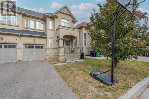 Side view of a beige townhouse with a driveway, grass, and a basketball hoop. - 59 Beachville Circle, Brampton