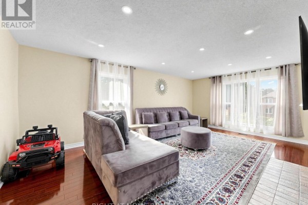 Living room with velvet sofas, ottoman, patterned rug, and hardwood floors - 59 Brennan Road Ajax