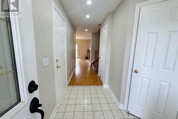 Hallway inside a townhouse with tiled and hardwood floors, white doors, and recessed lighting. - 59 Checkerberry Crescent, Brampton