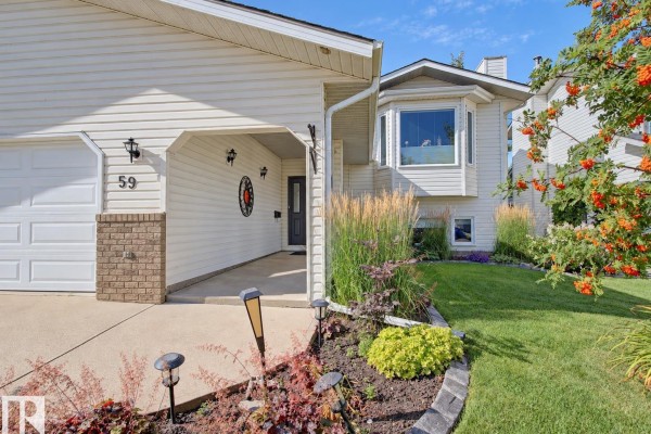 Close-up of the covered front entrance and bay window of a white house with landscaping. - 59 Cimmaron Wy, Sherwood Park