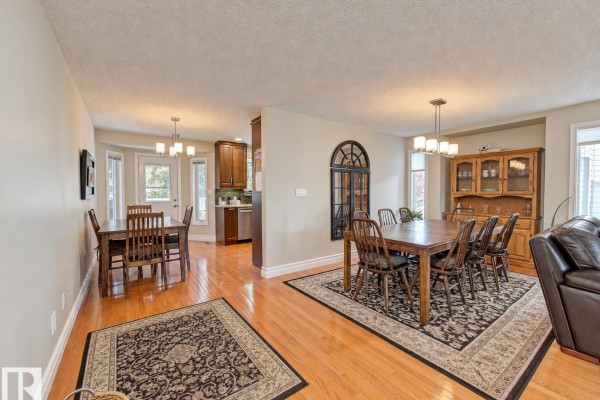 Open-concept living and dining area with hardwood floors, two dining tables, and decorative rugs. - 59 Cimmaron Wy, Sherwood Park