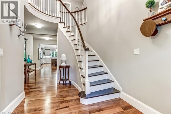 Interior foyer with a curved staircase, wood floors, and a view into the kitchen. - 59 Decou Road, Simcoe
