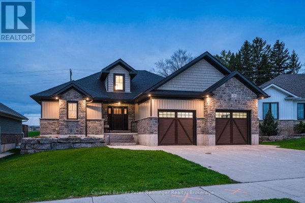 Dusk view of the front exterior of a modern house with stone and beige siding, a dark front door, and two double garage doors. - 59 Fischer Dairy Road, Brockton