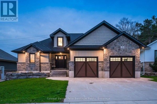 Dusk exterior view of a modern house, showcasing stone and beige siding, a pitched roof, and two brown wooden garage doors. - 59 Fischer Dairy Road, Brockton